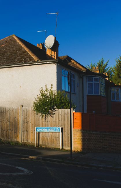 A collection of seven large cardboard boxes secured with plastic wrap and marked with 'FRAGILE' stickers, positioned on a brick doorstep outside a building with a brick wall and a closed, sliding glas